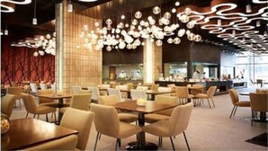 Un interior de restaurante moderno con mesas y sillas redondas, lámparas esféricas colgantes y una pared de ladrillo.