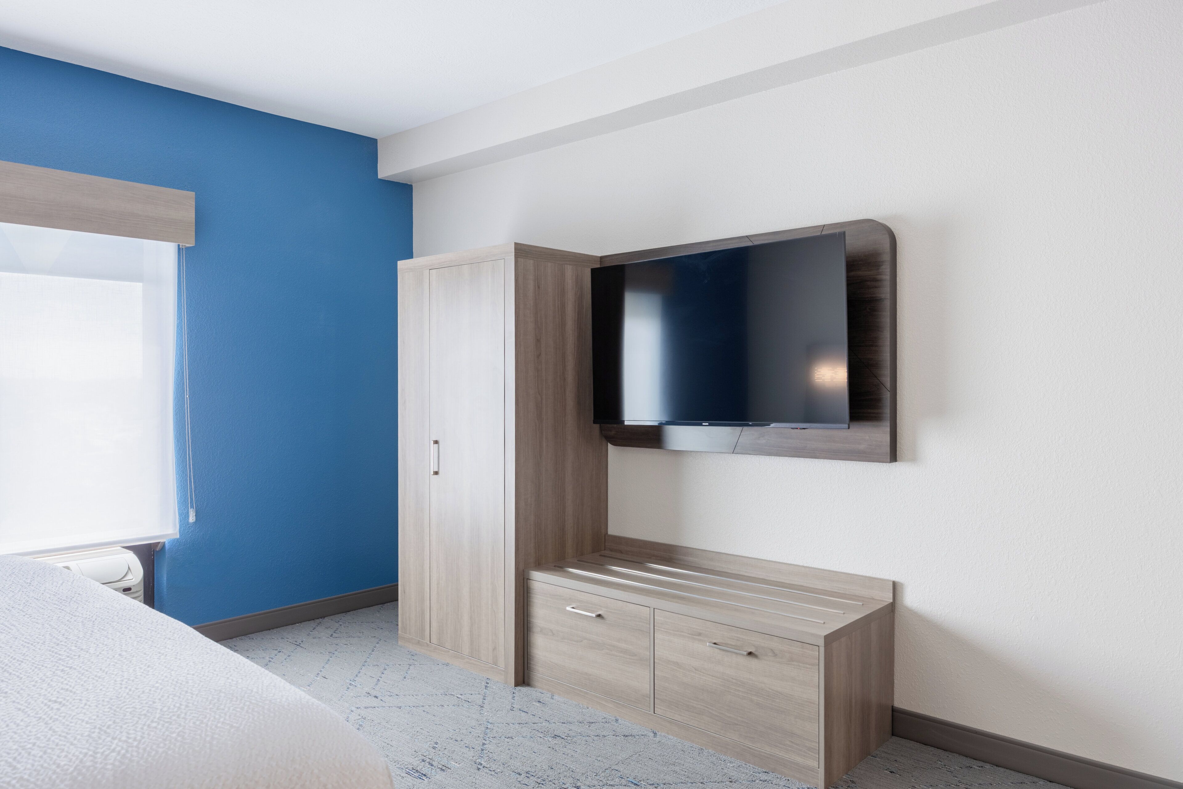 A bedroom with a bed, a wardrobe, a TV mounted on the wall, and a window.