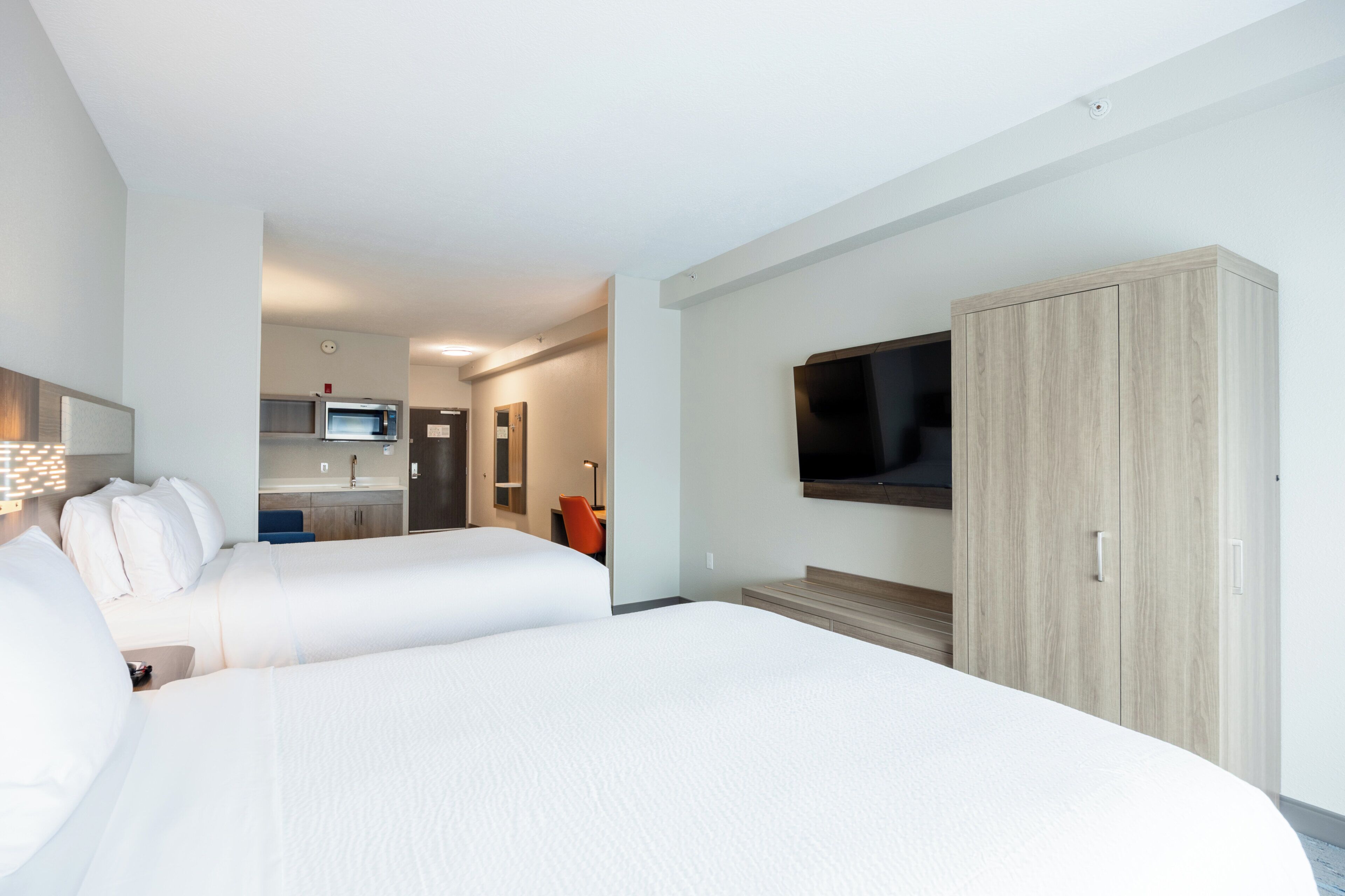 Ein Hotelzimmer mit zwei Betten, einem Fernseher, einem Holzschrank und einer Küchenzeile im Hintergrund.