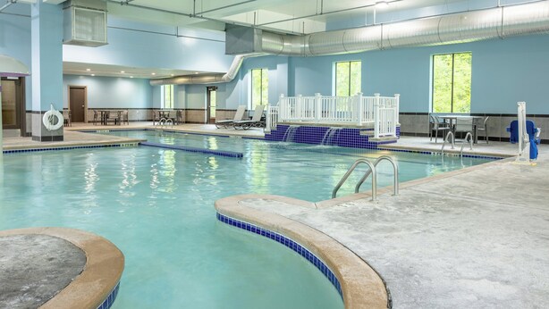Une piscine intérieure à l’eau d’un bleu limpide, dotée d’un plongeoir et d’un espace détente avec des tables et des chaises.