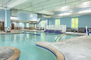 Una piscina interior con agua cristalina, un trampolín y una zona de estar con mesas y sillas.