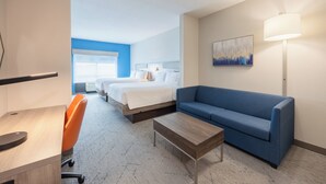 Une chambre d’hôtel avec un lit, un canapé bleu, un bureau avec une chaise, une lampe et un tableau au mur.