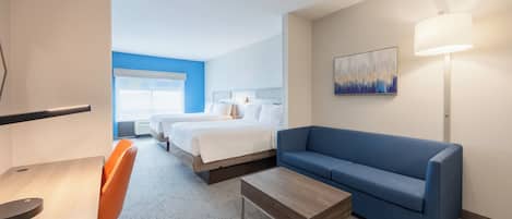 A hotel room with a bed, a blue sofa, a desk with a chair, a lamp, and a painting on the wall.