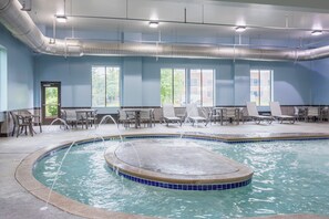 An indoor swimming pool with a tiled edge, lounge chairs, and a door leading outside. - Holiday Inn Express Hotels & Suites Columbus-Polaris Parkway by IHG (Columbus)