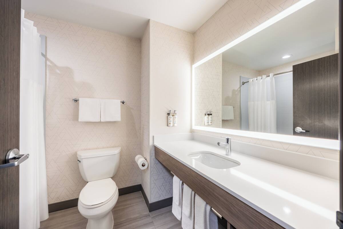 A modern bathroom with a toilet, sink, mirror, and towel rack.