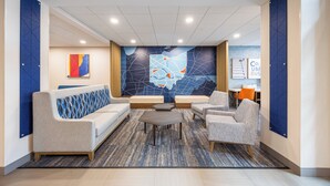 Un hall d’entrée comprenant un canapé, des fauteuils, une table basse, une carte géographique murale et un panneau indiquant « COLUMBUS BUS ».