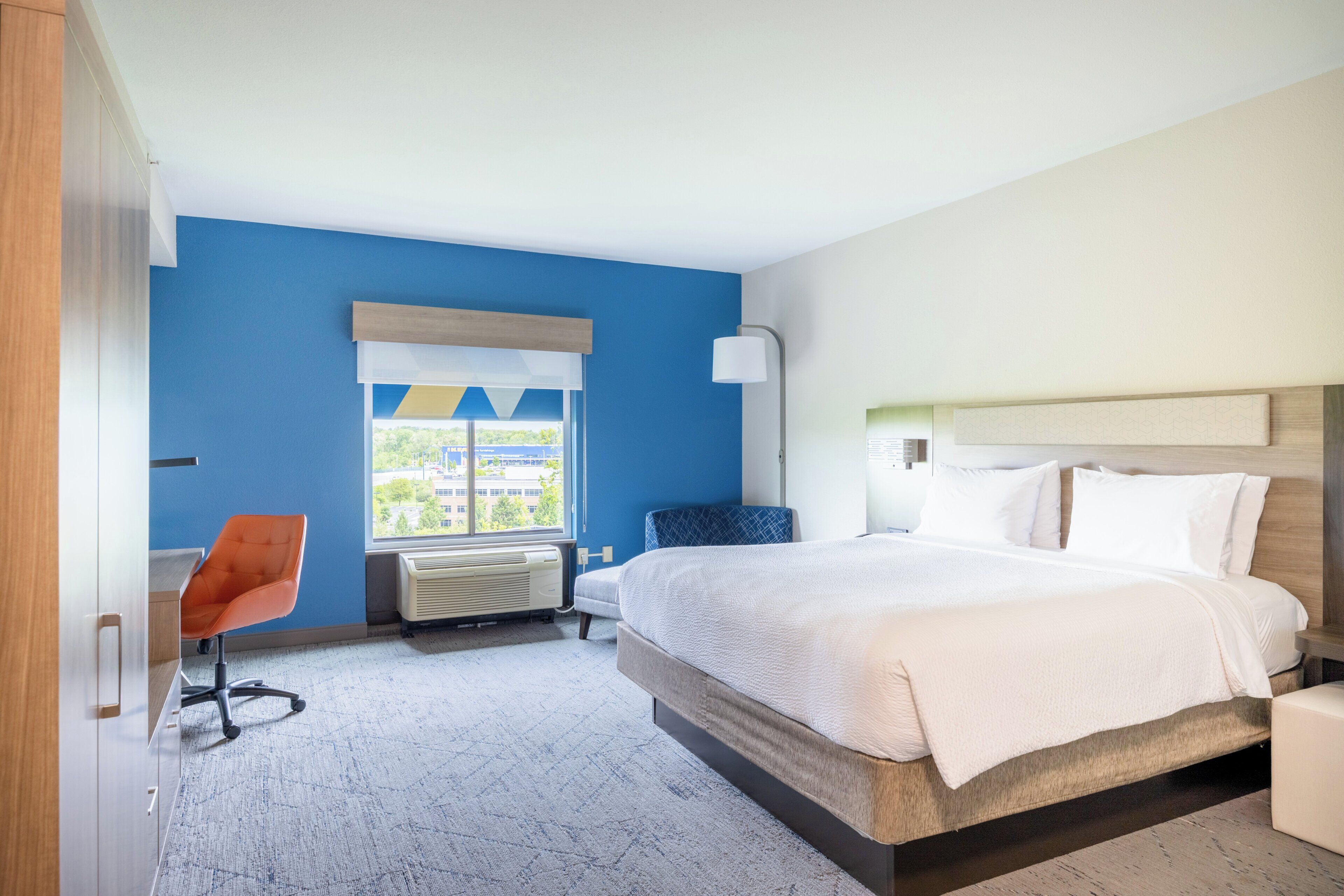 Ein Hotelzimmer mit Bett, Schreibtisch, einem orangefarbenen Sessel, einem Fenster mit Blick und einer Lampe.