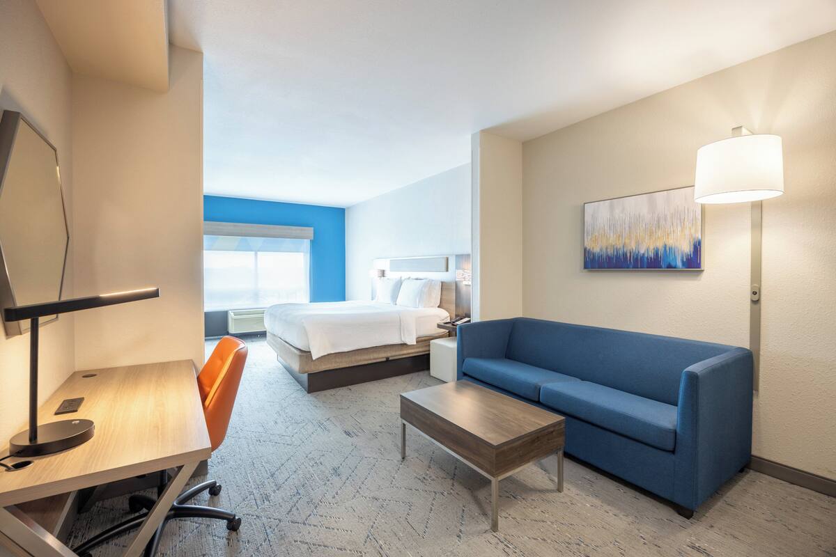 Una camera d'albergo con un letto, un divano blu, una scrivania con una lampada e un quadro appeso al muro.