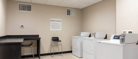 A guest laundry area with a sign, two washing machines, a dryer, a small table, and two stools.