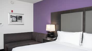 Quarto de hotel com uma cama, mesa de cabeceira, abajur, sofá e um quadro na parede.