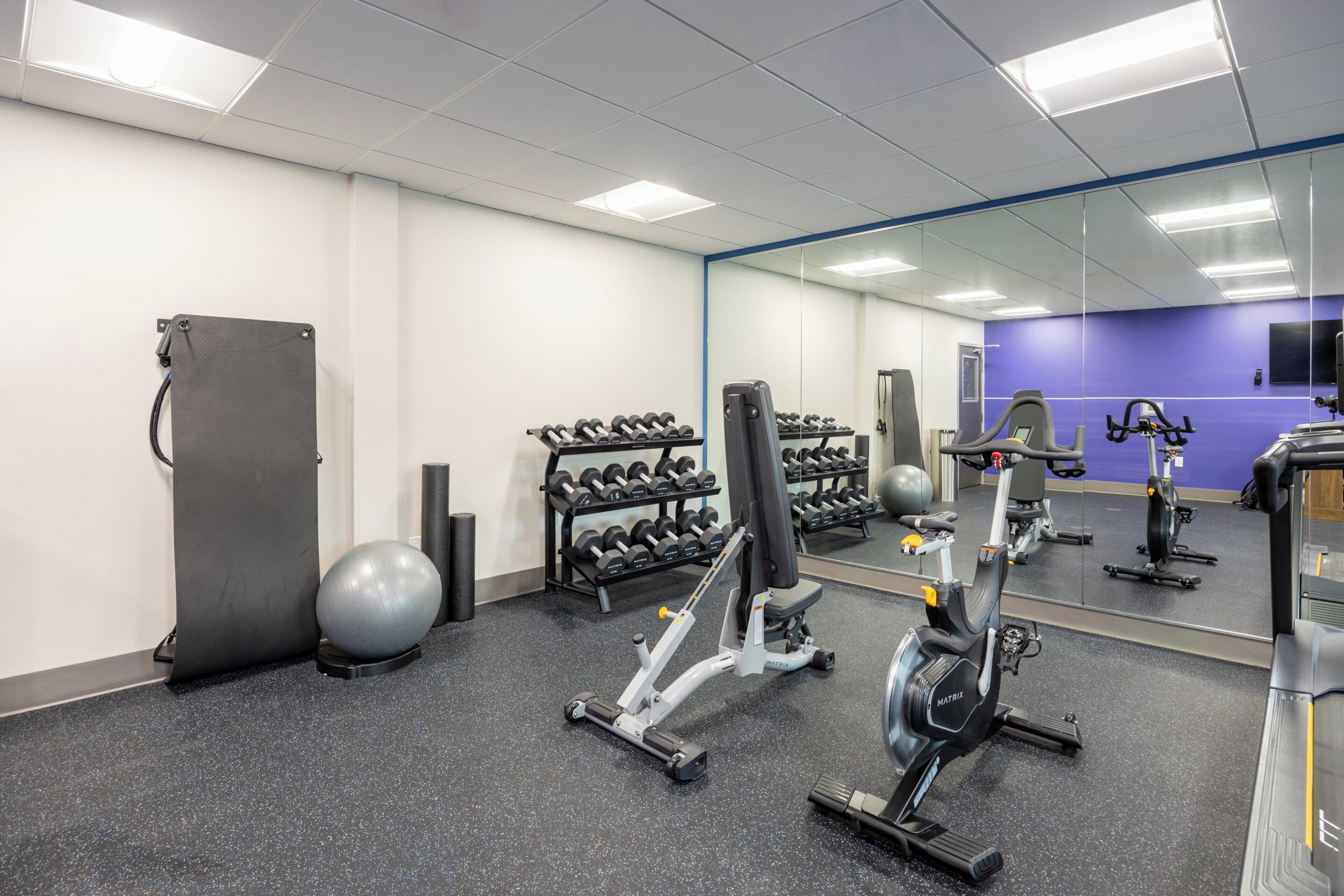 A gym with exercise equipment, a mirrored wall, and a purple wall.