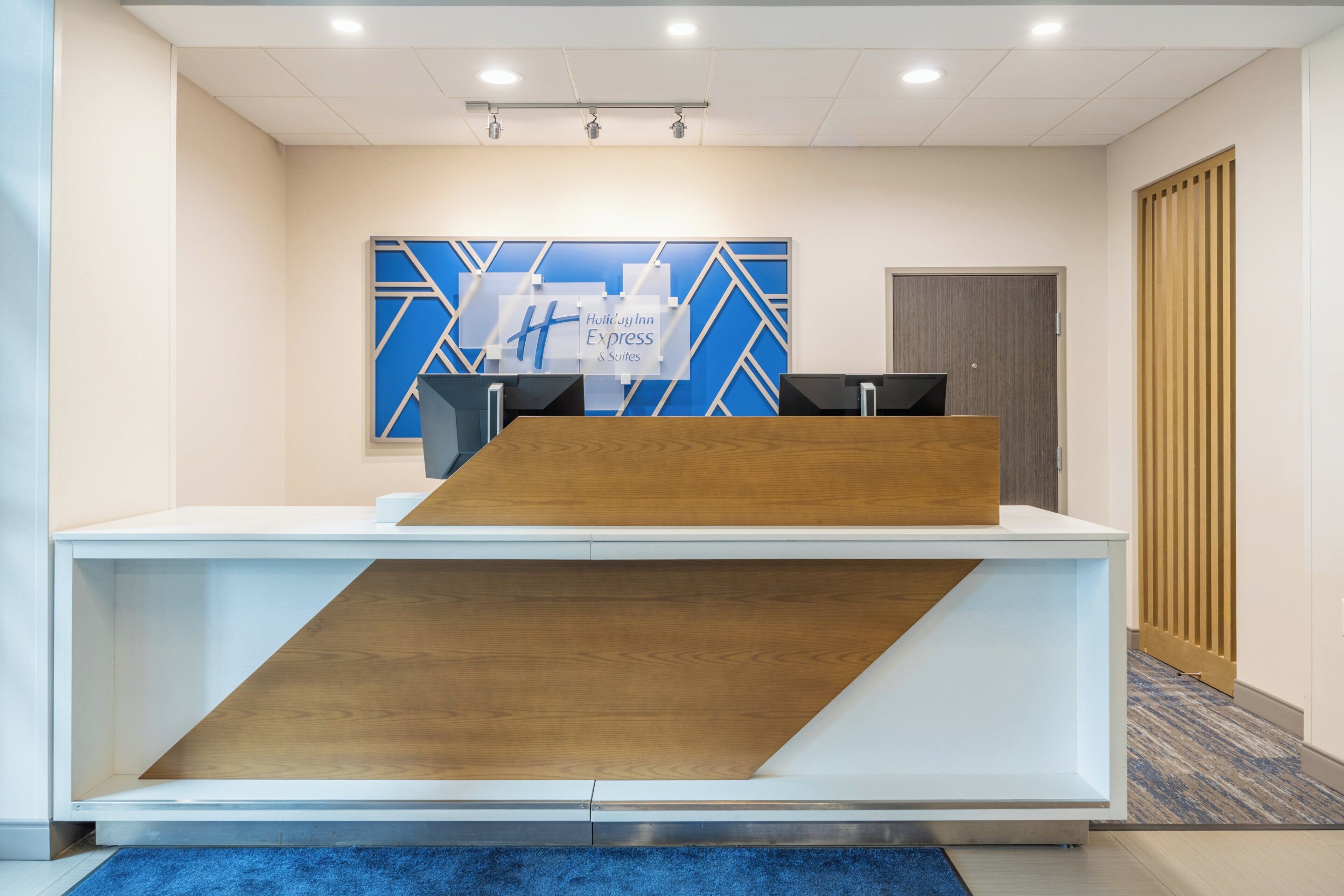 Un mostrador de recepción con diseño moderno, un cuadro de pared geométrico azul y blanco, y un detalle de madera.