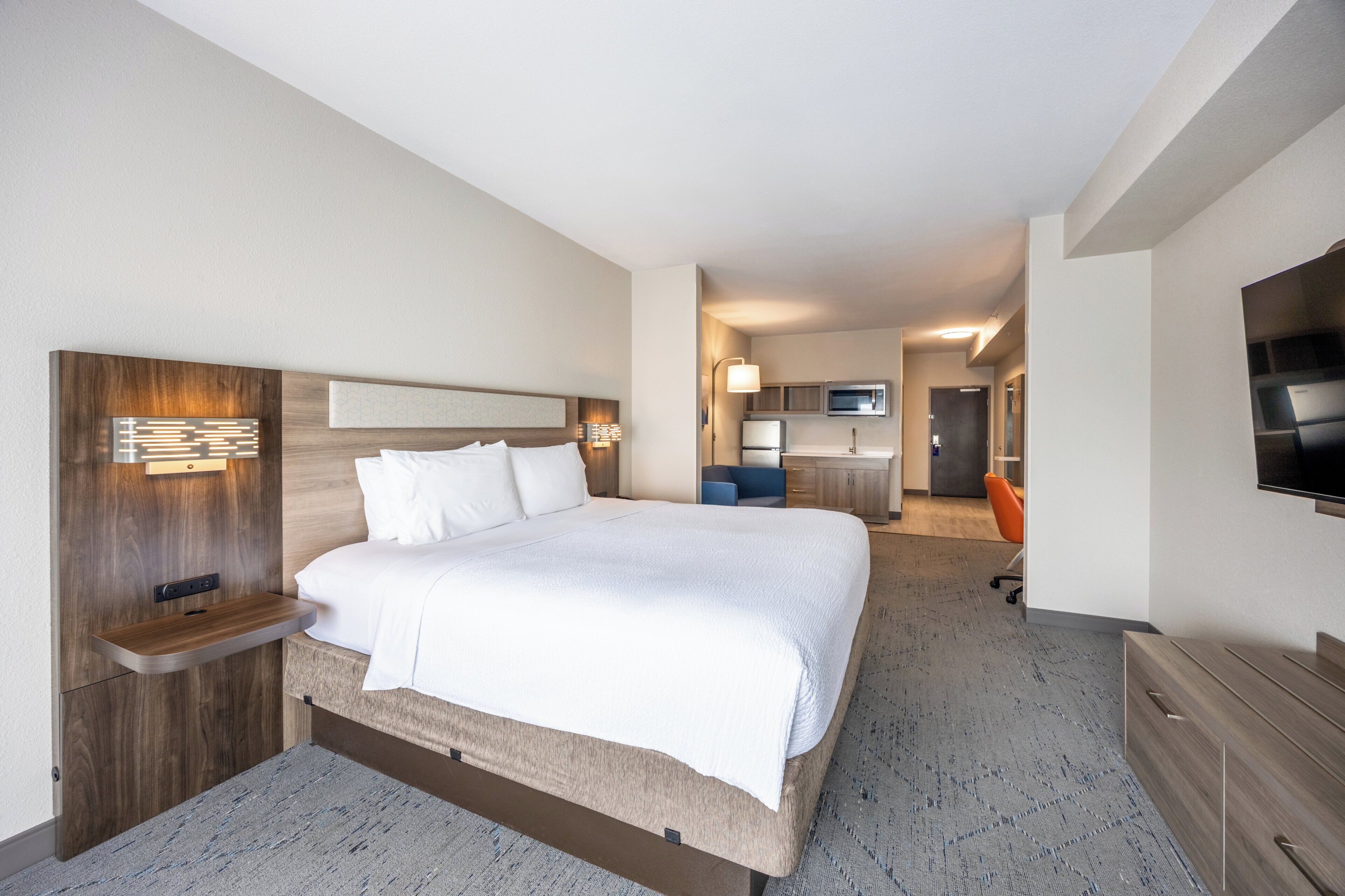 Ein Hotelzimmer mit einem großen Bett, Nachttischen, einem Flachbildfernseher, einem Schreibtisch und einer Küchenzeile.
