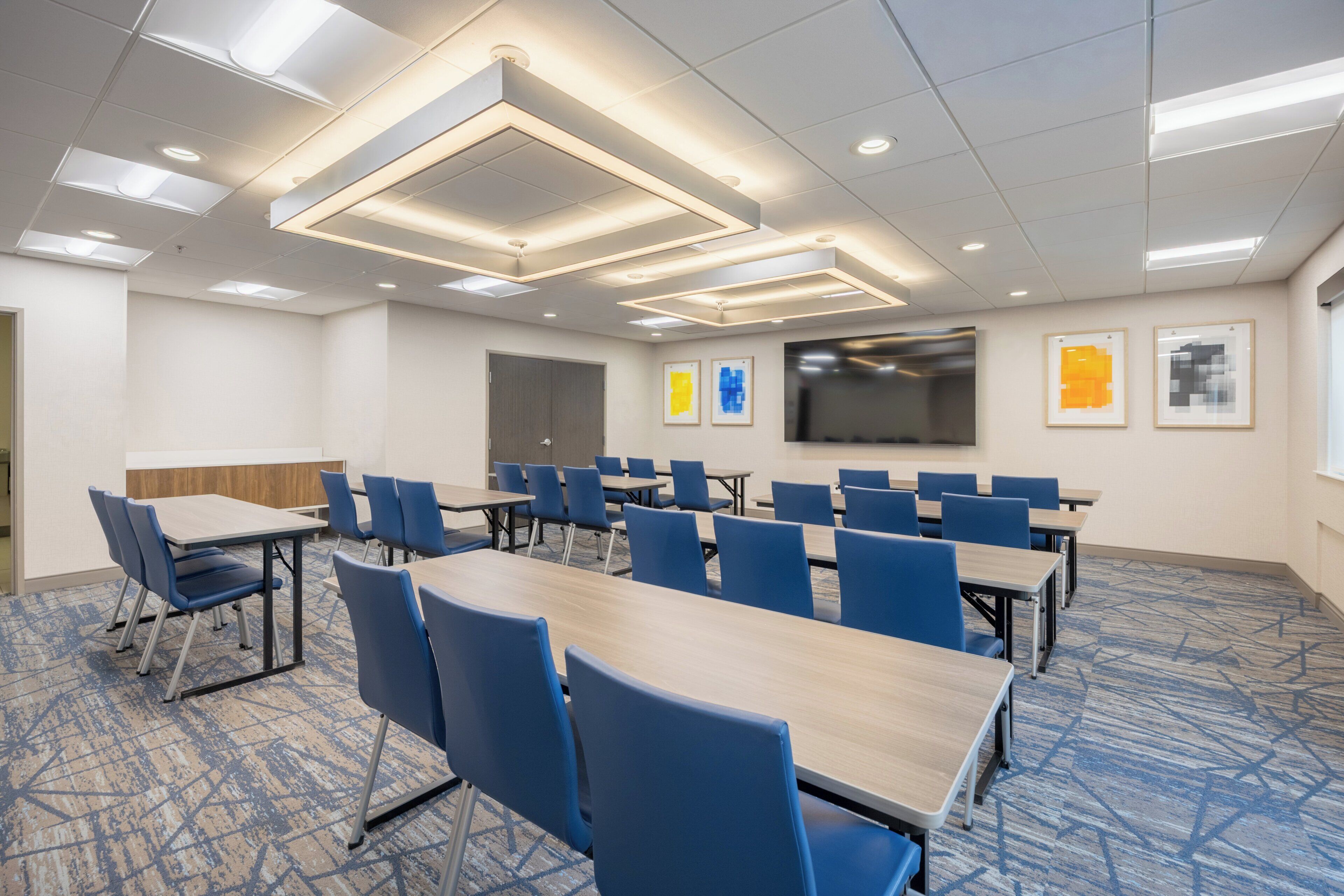 A conference room with tables and chairs, a flat-screen TV, and framed artwork on the walls.