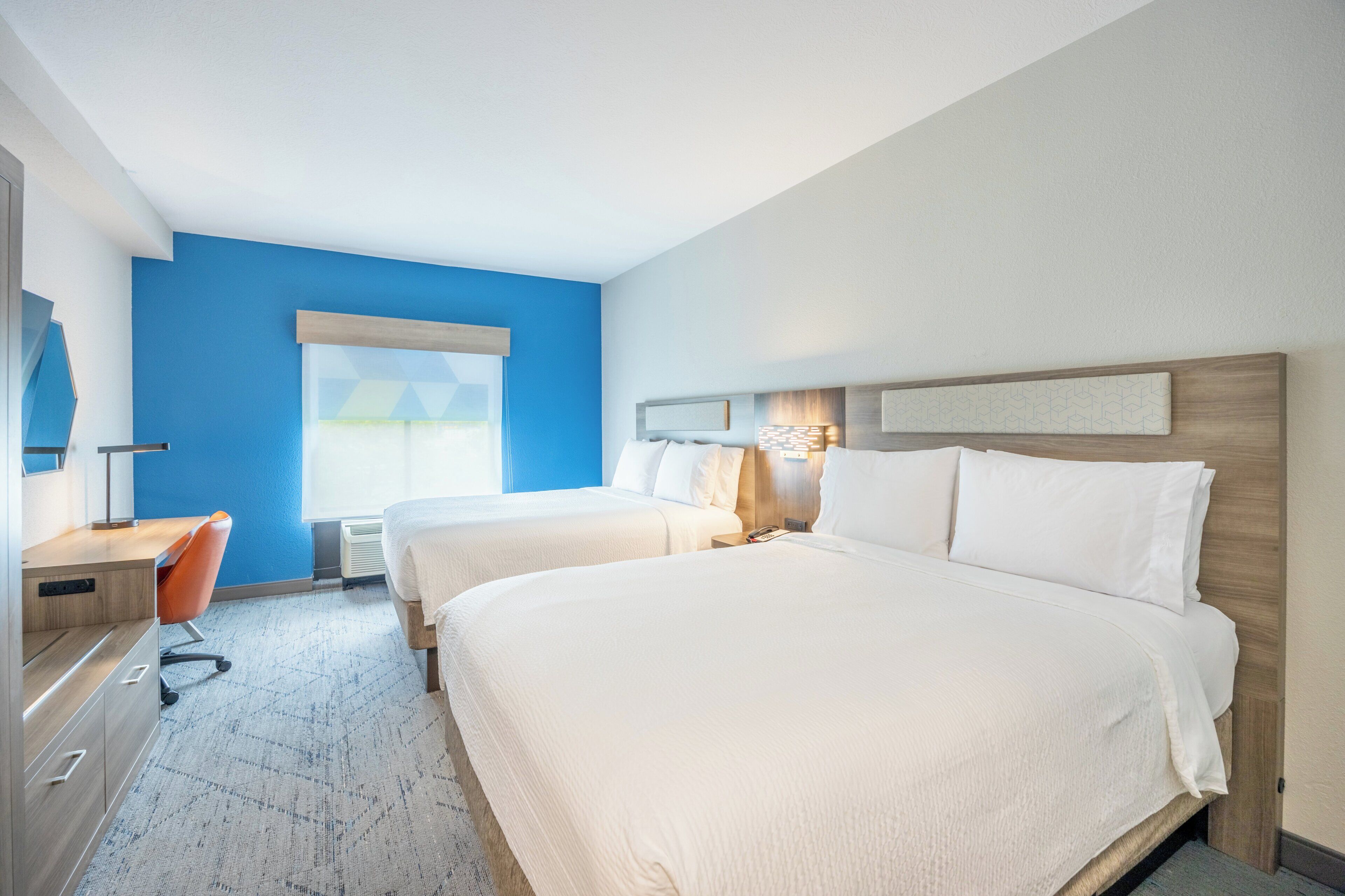 Ein Hotelzimmer mit zwei Betten, einem Schreibtisch, einem Stuhl und einem Fenster mit Jalousien.