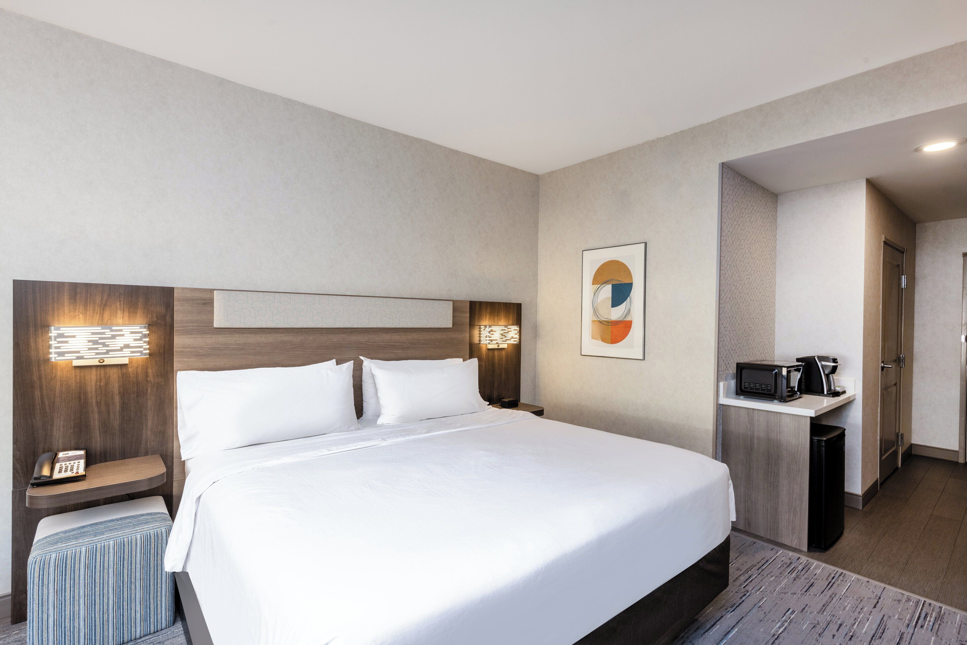 A hotel room with a large bed, bedside tables, a desk with a coffee maker, and a microwave.