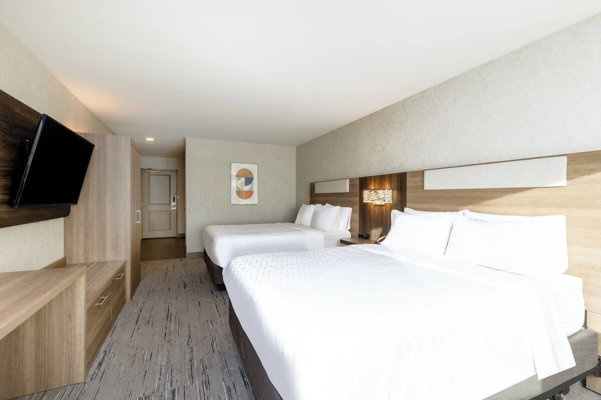 A hotel room with a large bed, a TV mounted on the wall, and a wooden headboard.