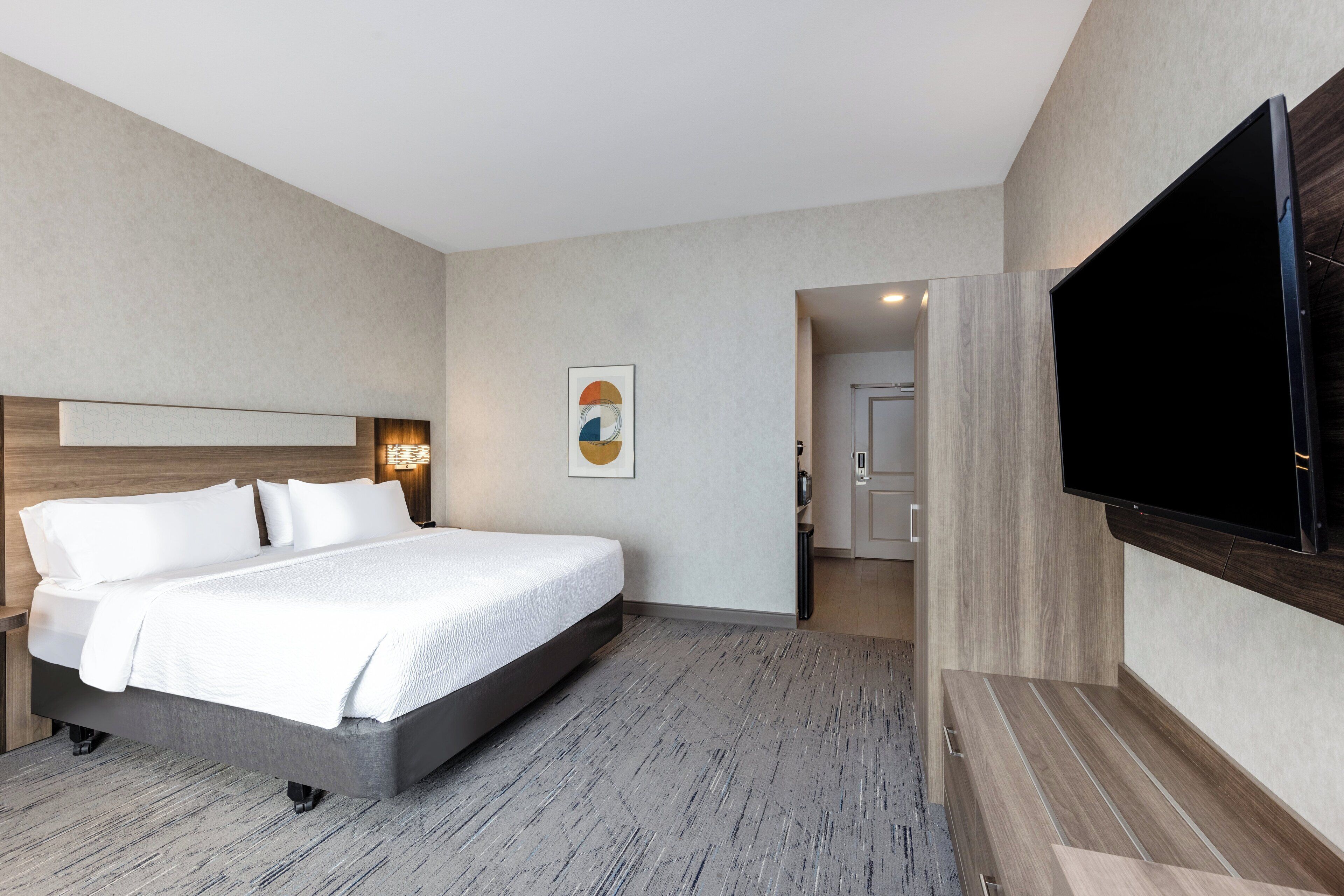 A modern hotel room with a large bed, a flat-screen TV mounted on the wall, and a minimalist design.