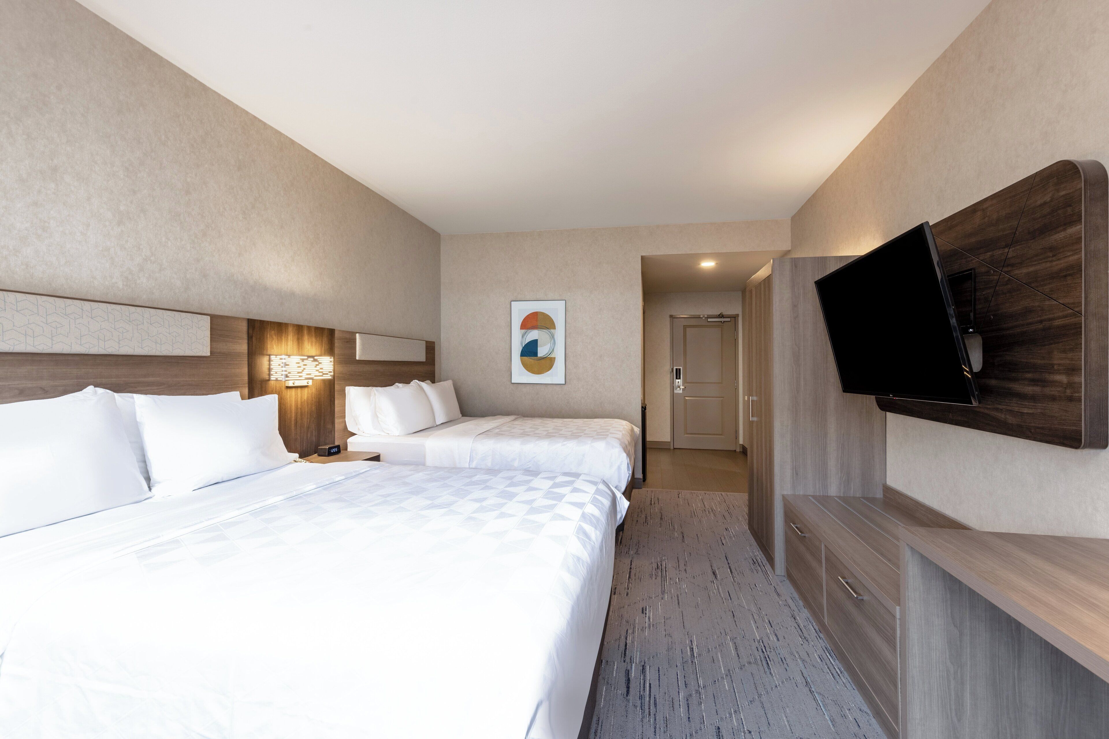 Habitación de hotel con dos camas, un televisor de pantalla plana en la pared y un escritorio pequeño con cajones.