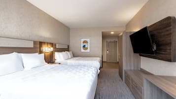 Habitación de hotel con dos camas, un televisor de pantalla plana en la pared y un escritorio pequeño con cajones.
