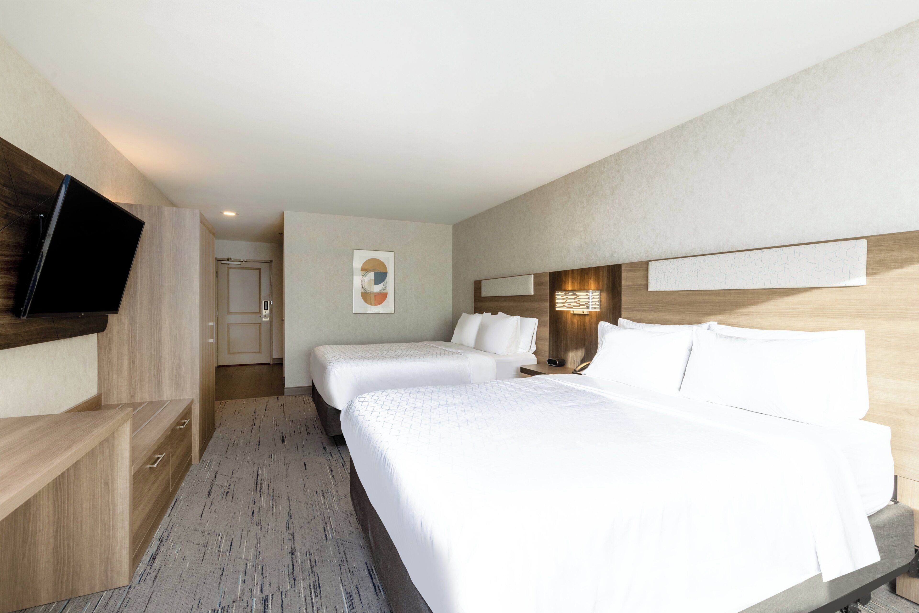 Une chambre d’hôtel avec un grand lit, un téléviseur fixé au mur et une tête de lit en bois.