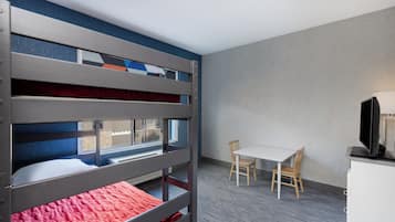 A bunk bed room with a desk and chairs, a television, and a window.