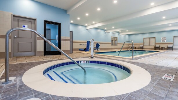 Un espace piscine comprenant un jacuzzi, un vestiaire et une porte signalée par des pictogrammes d’accessibilité.