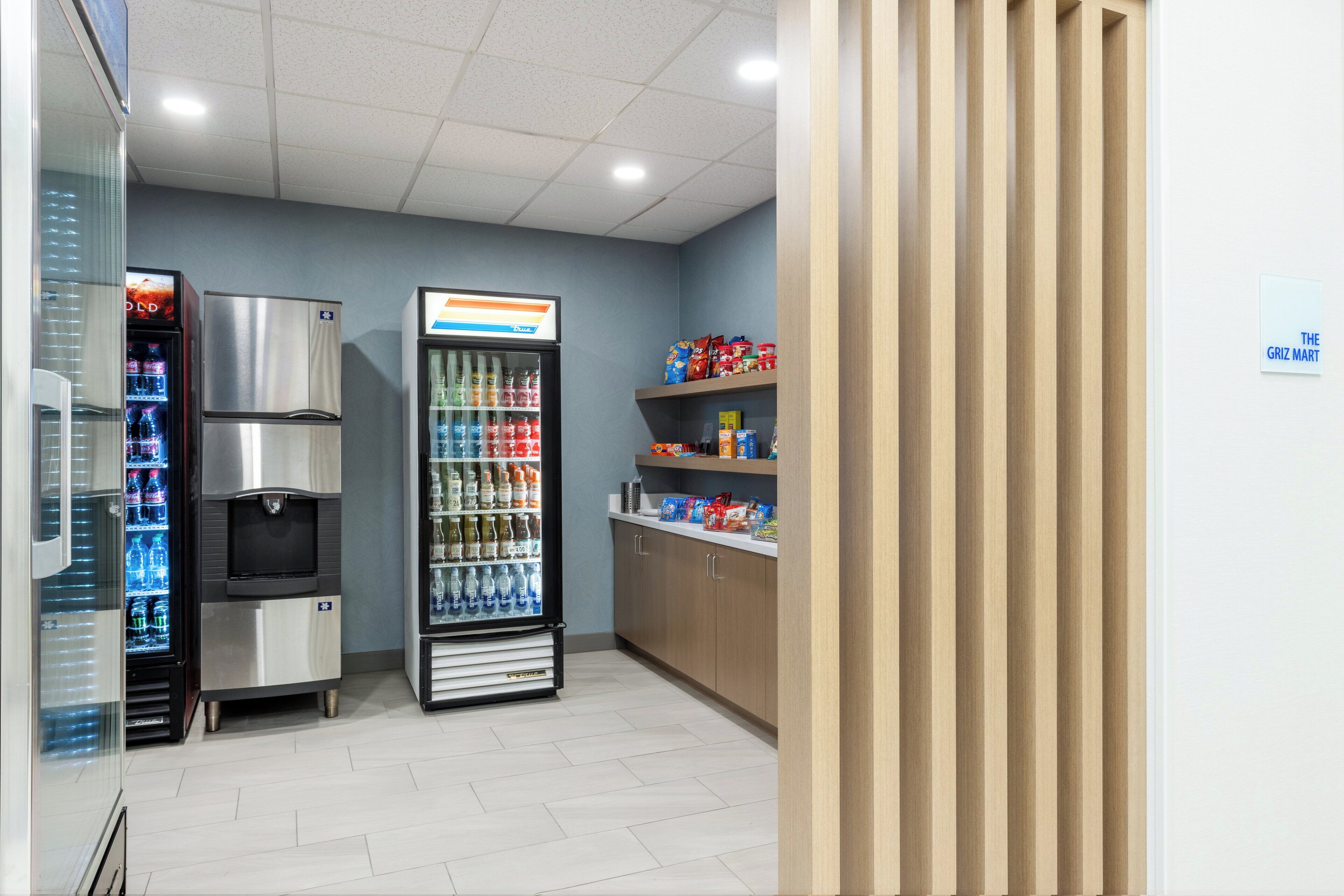A clean, modern interior with a self-service beverage dispenser, refrigerated display cases, and a wooden counter with snacks.