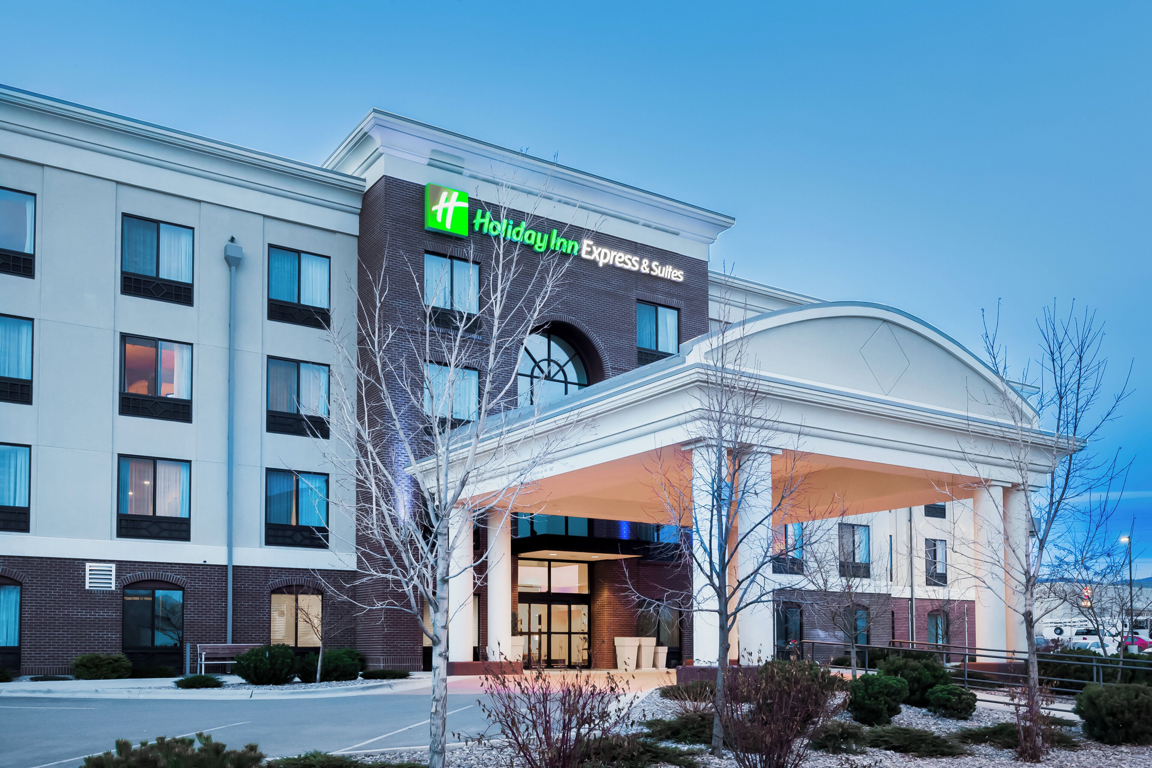 Et Holiday Inn Express & Suites hotel med en moderne facade, store vinduer og et overdækket indgangsparti.