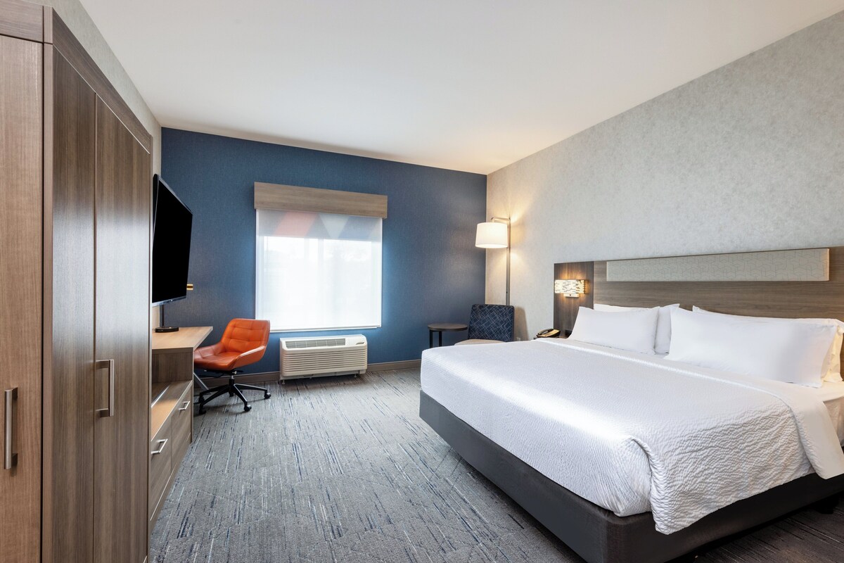 A hotel room with a large bed, a desk with a chair, a television, and a window with blinds.