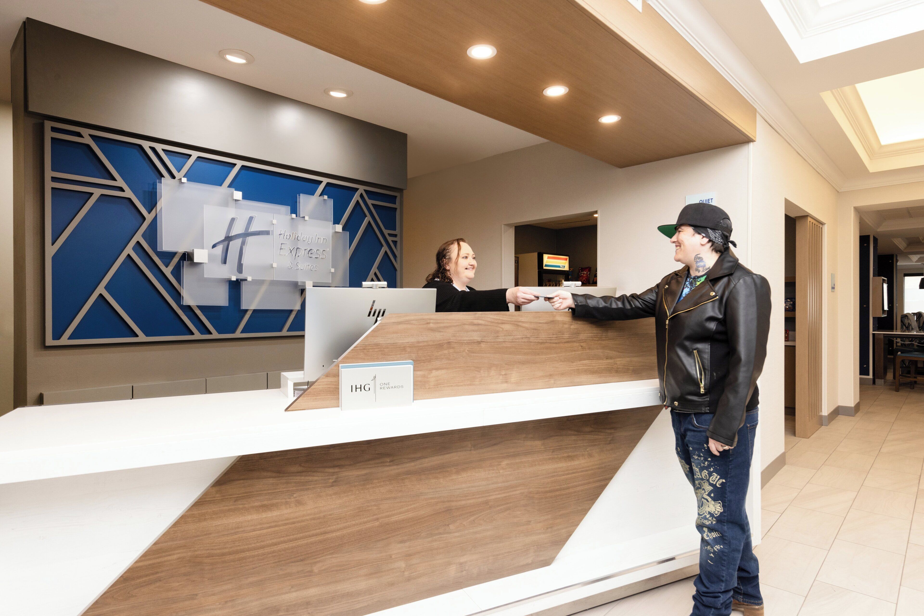 A hotel reception desk with a modern design, a digital screen, and a sign indicating a loyalty program.