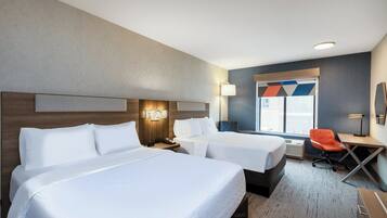 A hotel room with two beds, a desk, an orange chair, and a window with a view.