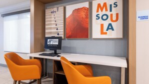 Un comptoir d’accueil d’hôtel avec deux chaises orange, un écran d’ordinateur et des œuvres d’art encadrées accrochées au mur.