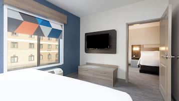 A hotel room with a bed, a TV mounted on the wall, a dresser, and a window with a geometric view.