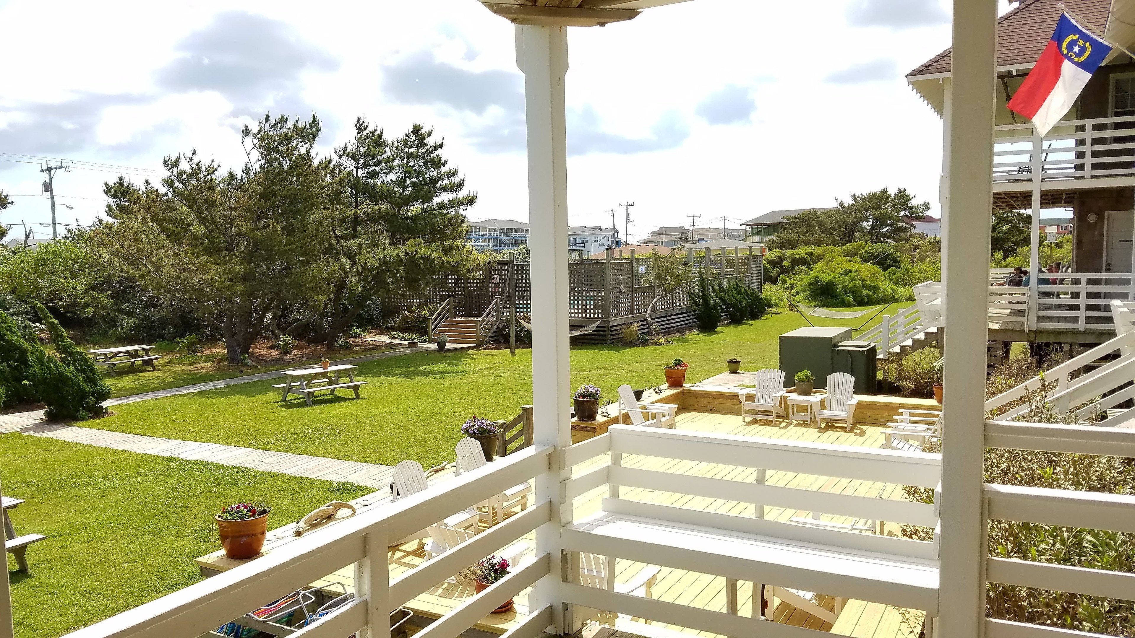 A balcony with a view of a well-maintained garden, outdoor seating, and a flag.