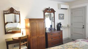 A bedroom with a bed, a wooden dresser, a desk with a chair, a mirror, and a door.