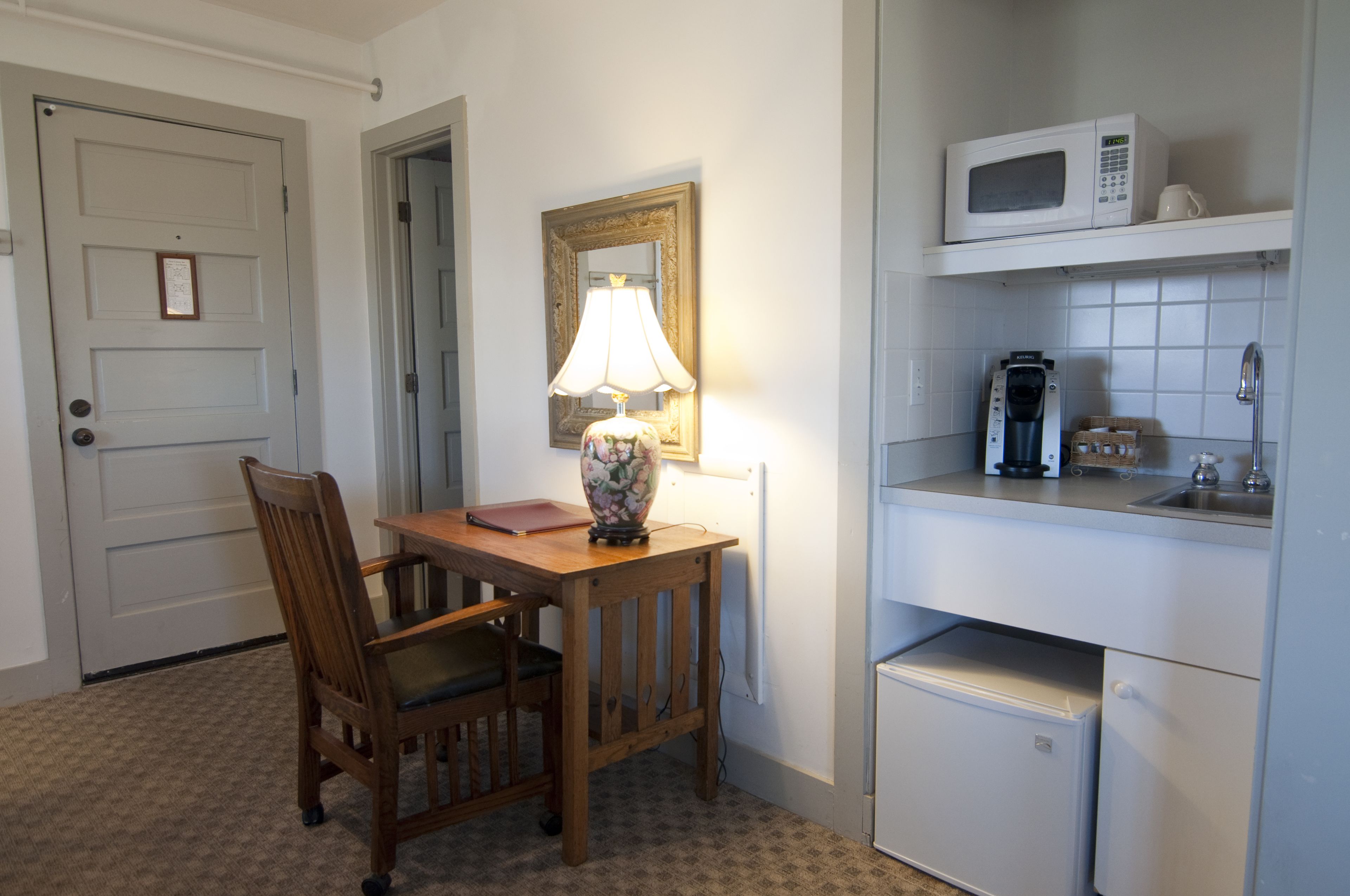 Una cocina compacta con una mesa y silla de madera, una lámpara, un microondas y una cafetera.