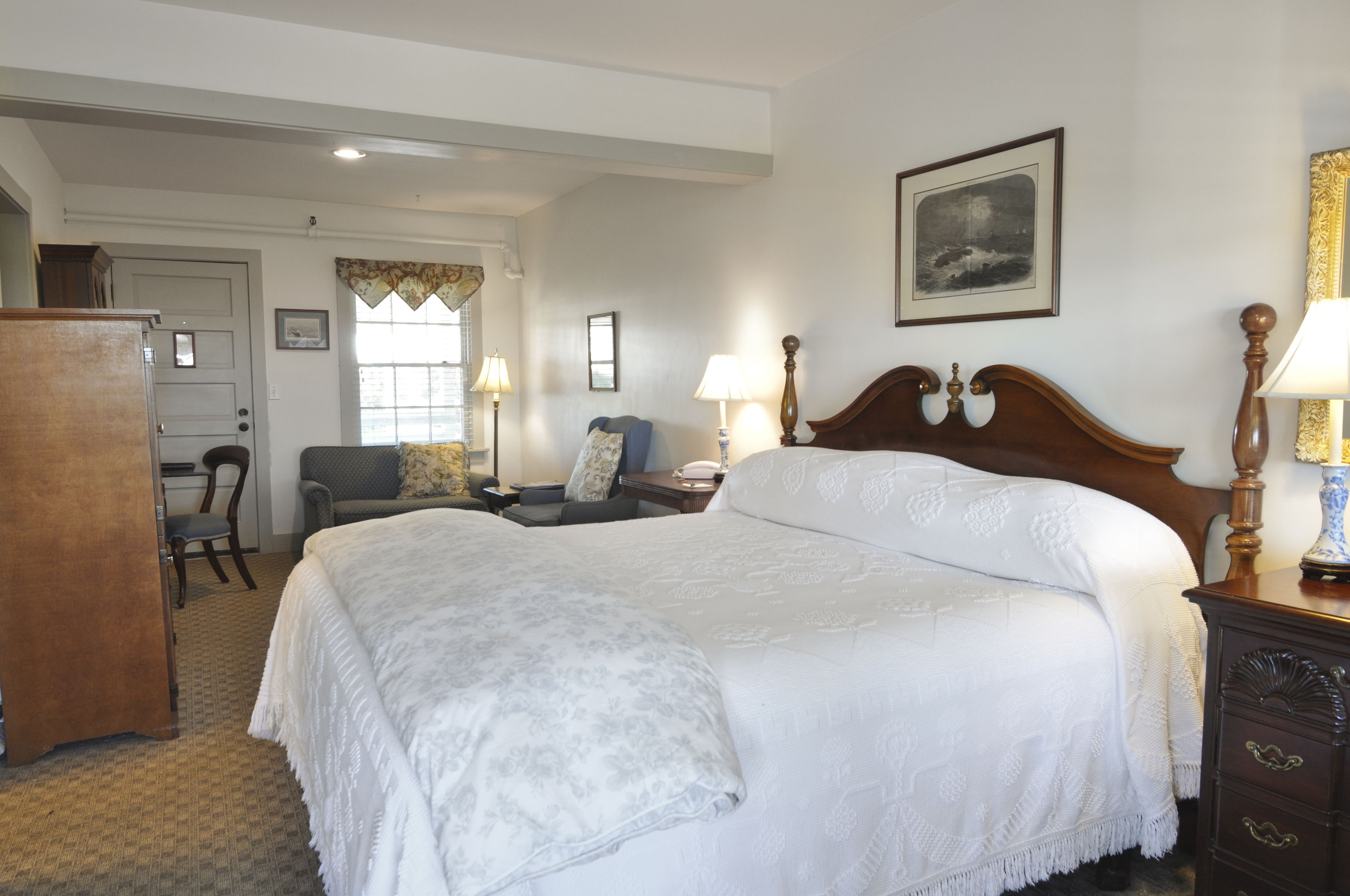 A hotel room with a large bed, a desk, a chair, a dresser, and a window with curtains.