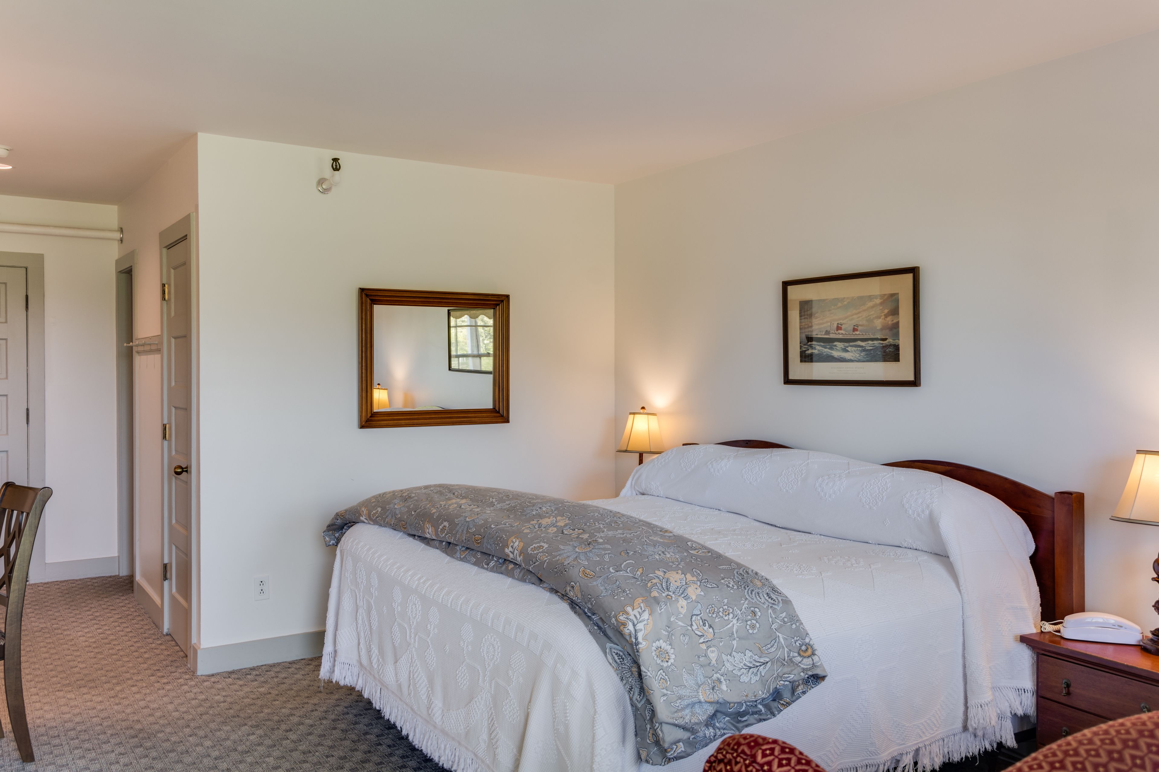 A bedroom with a bed, bedside lamps, a framed picture, and a door leading to another room.