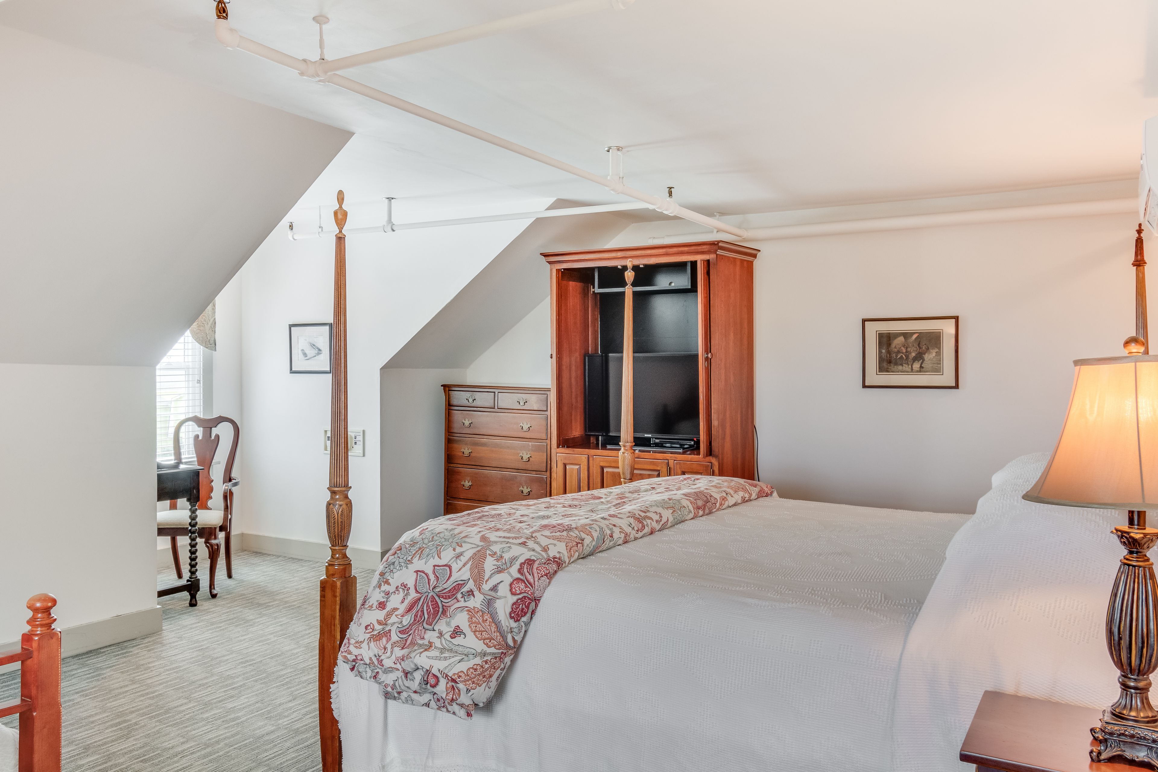 Un dormitorio con una cama grande, un armario de madera, un televisor y un escritorio con una silla.