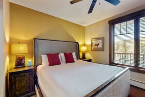 A hotel room with a large bed, two bedside lamps, a nightstand, a framed picture, and a window with blinds. - Water House on Main Street (Breckenridge)