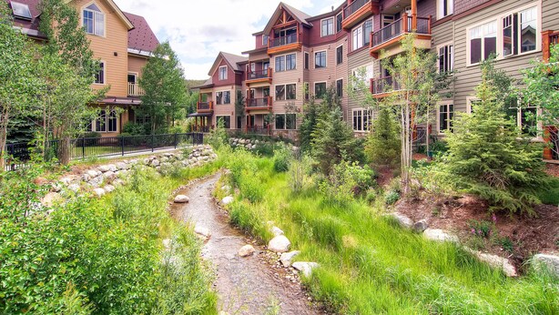 A residential area with multi-story houses, a small stream, and surrounding greenery. - Water House on Main Street (Breckenridge)