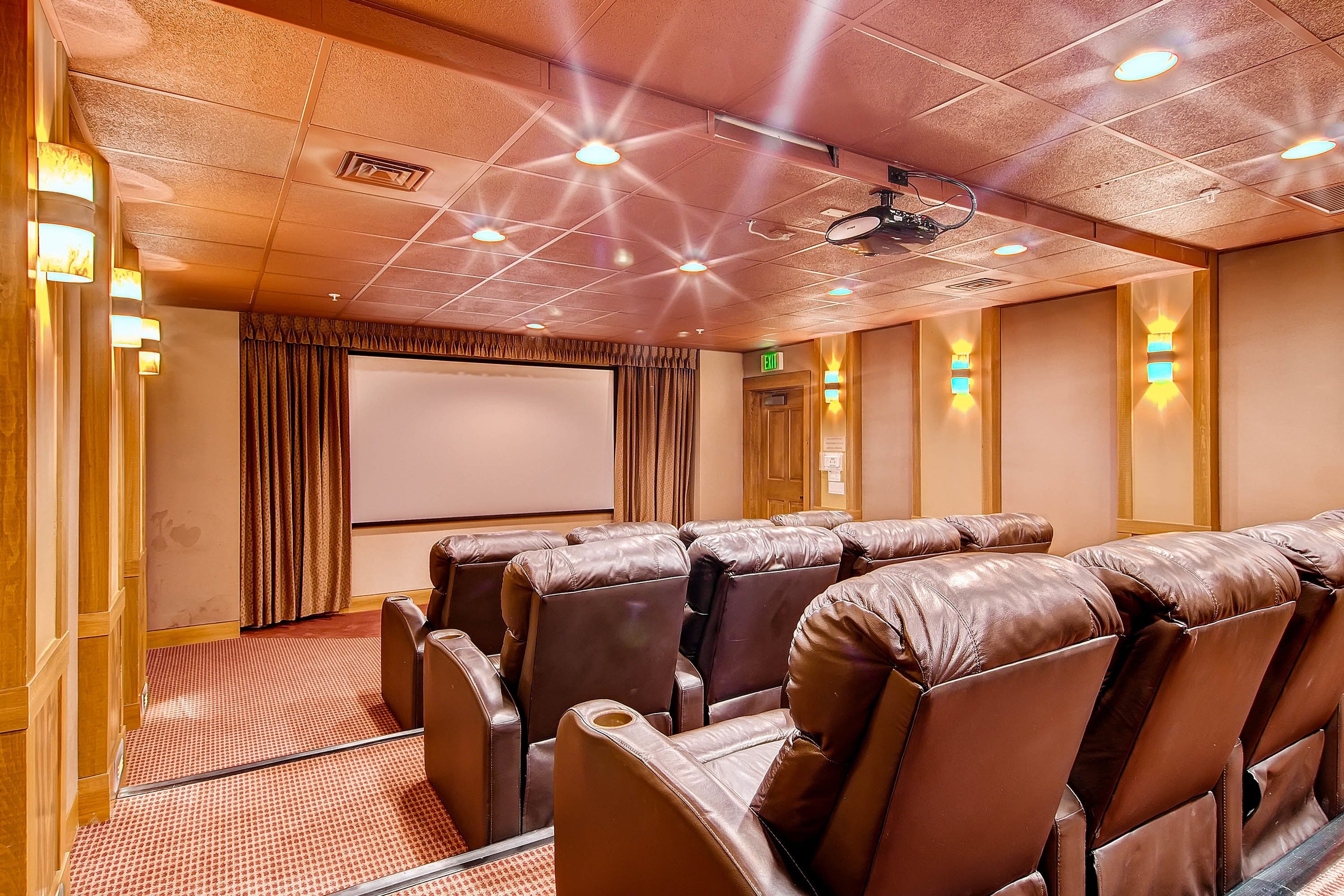 A theater room with leather reclining seats, a large screen, and ceiling lights.