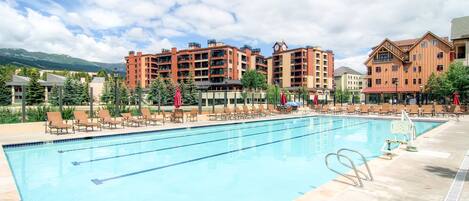 A swimming pool with lounge chairs and umbrellas, surrounded by multi-story buildings with balconies.