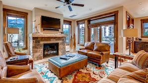 A spacious living room with leather furniture, a stone fireplace, and large windows offering mountain views. - Water House on Main Street (Breckenridge)