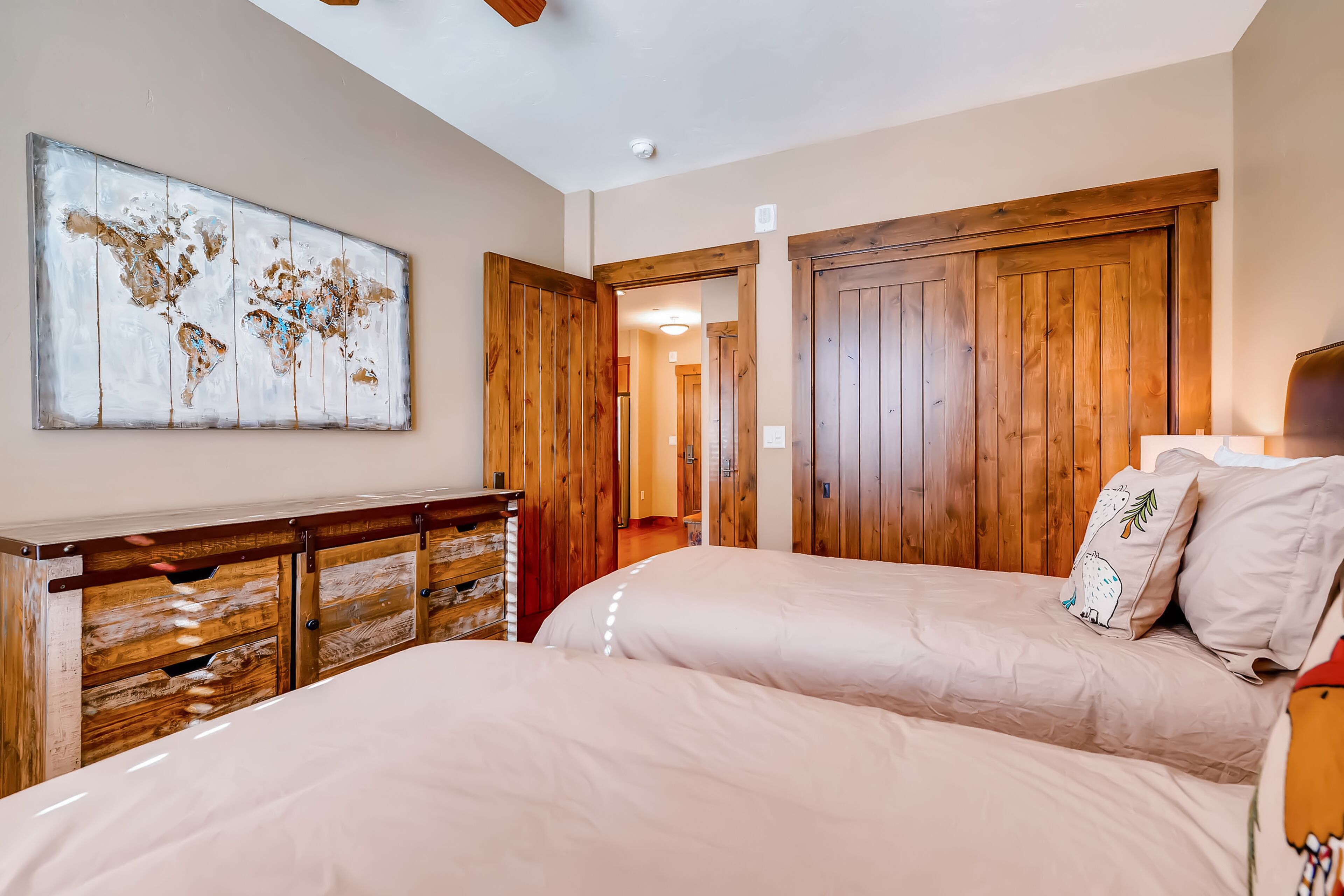 A bedroom with two beds, wooden wardrobe, and a world map artwork.