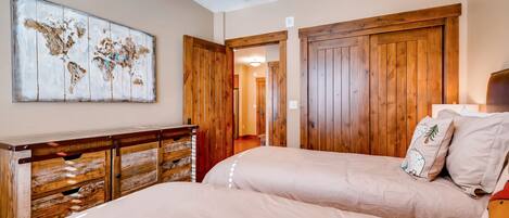 A bedroom with two beds, wooden wardrobe, and a world map artwork.