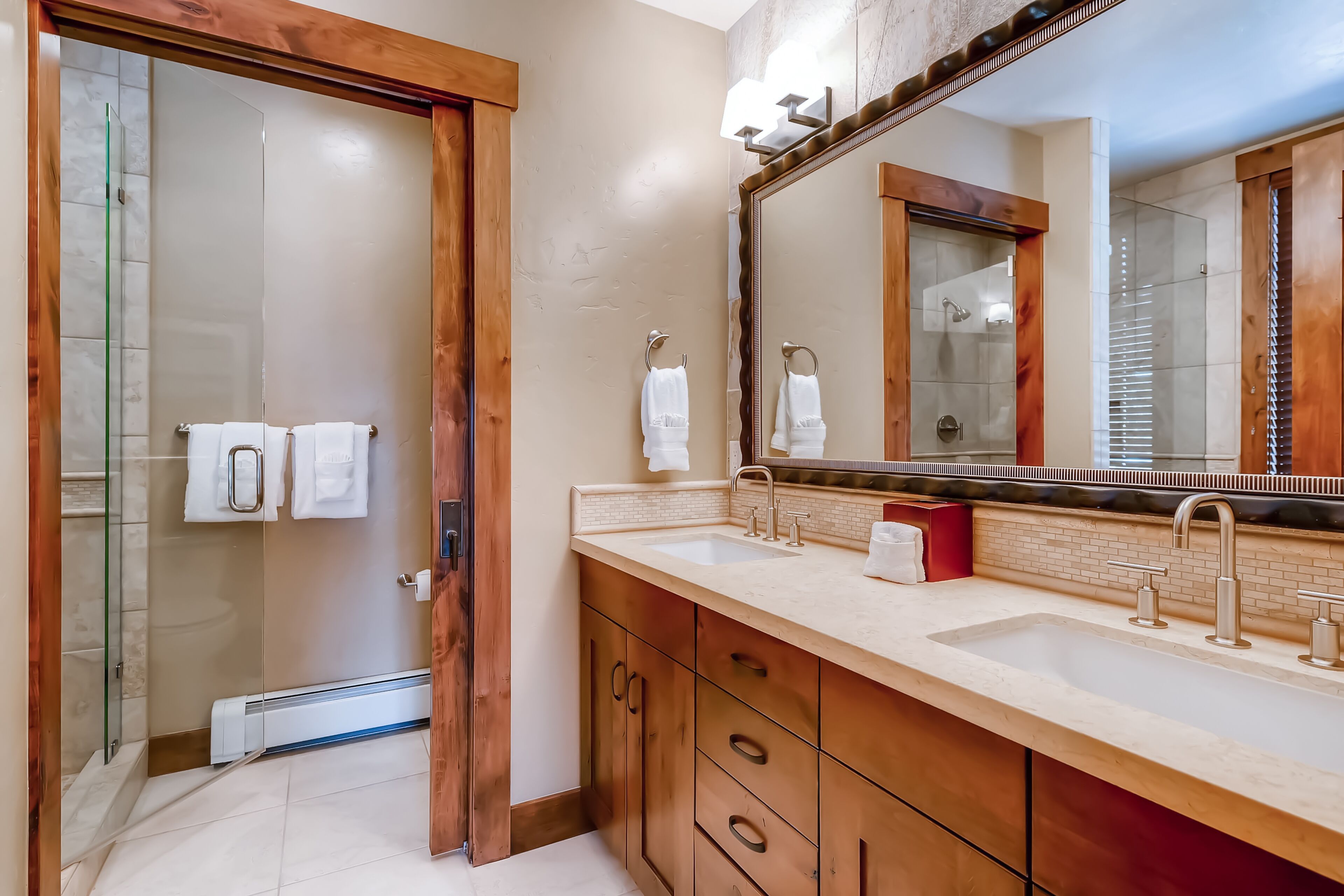 A modern bathroom with a large mirror, a double sink, and a glass shower enclosure.
