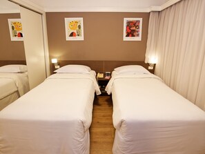 A hotel room with two single beds, a bedside table with a lamp, a phone, and artwork on the wall.