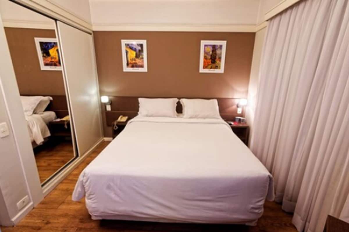 A hotel room with a large bed, a bedside table with a lamp, and a mirror on one wall.